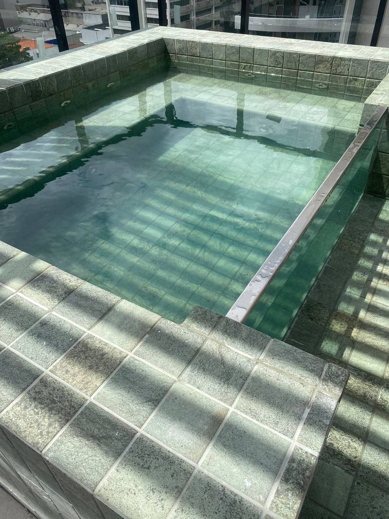 Detalhe da água do spa de cerâmica vista de cima, com o revestimento verde e o vidro frontal